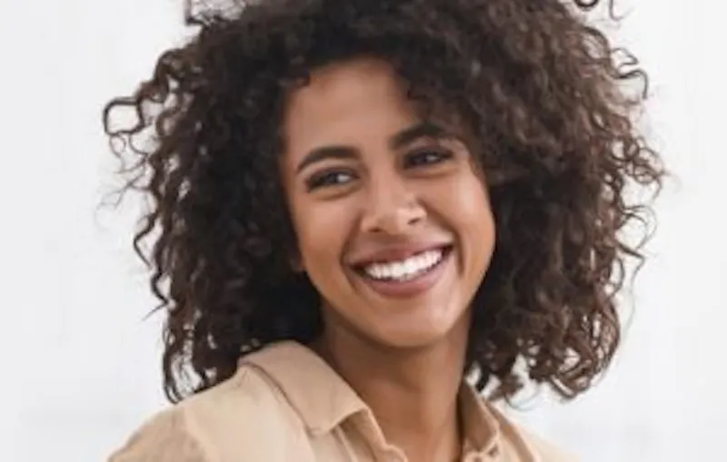 smiling woman with curly hair and a tan shirt
